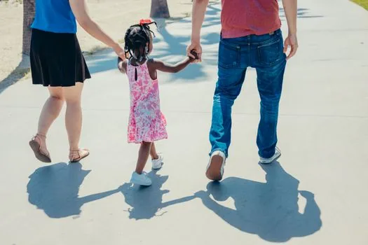 accessible amusement park pathway with family and caregiver walking together in daylight, hopeful community news photography, no readable signage or logos