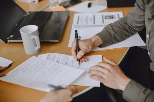 actor and community representative signing an agreement document on a simple table, amusement park map blurred in background, realistic Korean editorial photo, no readable text