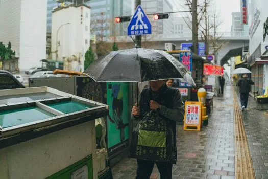 close view of drainage workers and emergency responders inspecting a blocked roadside drain in heavy rain, Korean coastal town, documentary photo, no text