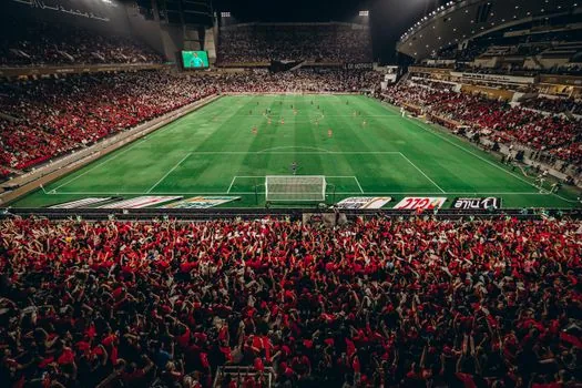 night football stadium in Monaco after final whistle, red and white players celebrating near a 2-0 scoreboard, realistic sports editorial photo