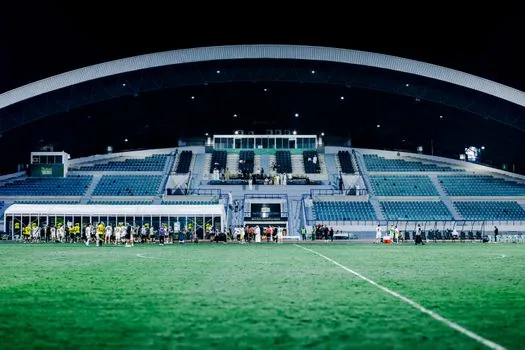 night football stadium scoreboard showing four to one result, press area laptop with generic league table, editorial sports photography, no logos, no real players