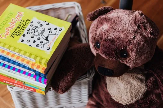 stack of children's books with a small guitar and white flowers on a wooden table, warm library light, respectful tribute to literacy philanthropy