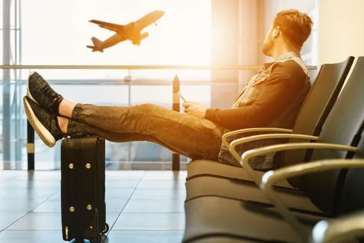 airline passenger checking delay notice on smartphone beside airport departure board, boarding pass and suitcase nearby | 항공편 지연 사유 확인 장면 | 지연·결항 안내를 먼저 확인하는 상황