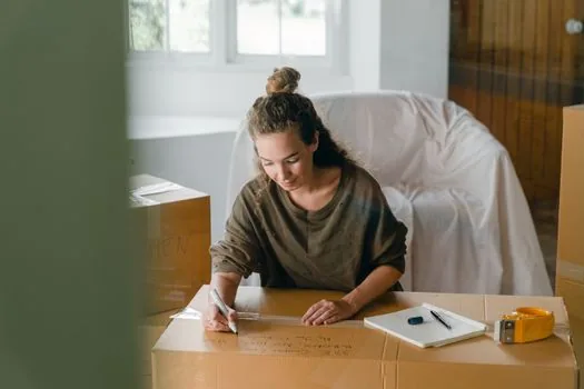 family member sending household head confirmation request on phone, laptop with official form style interface, moving boxes, calm home interior