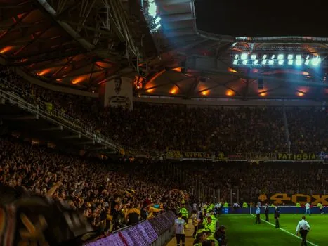 football scoreboard showing 2-3 result at a night stadium, green white home crowd, white away team mood, no real logos, editorial sports lighting