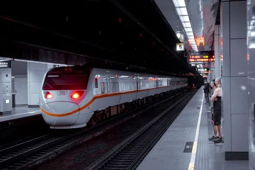 Korean high speed rail passenger checking partial refund notification on smartphone near station platform delay board, realistic bright transportation guide photo, no visible brand logos, no personal data | 지연배상 자동 환급 알림을 확인하는 장면