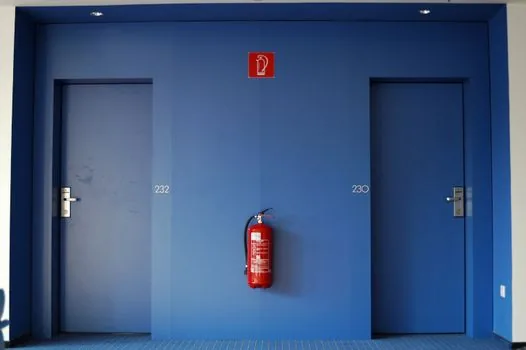 person filling safety report on smartphone beside emergency exit sign and building hallway, realistic public safety documentation photo | 안전신문고에 위치와 사진을 첨부해 신고 내용을 정리하는 장면